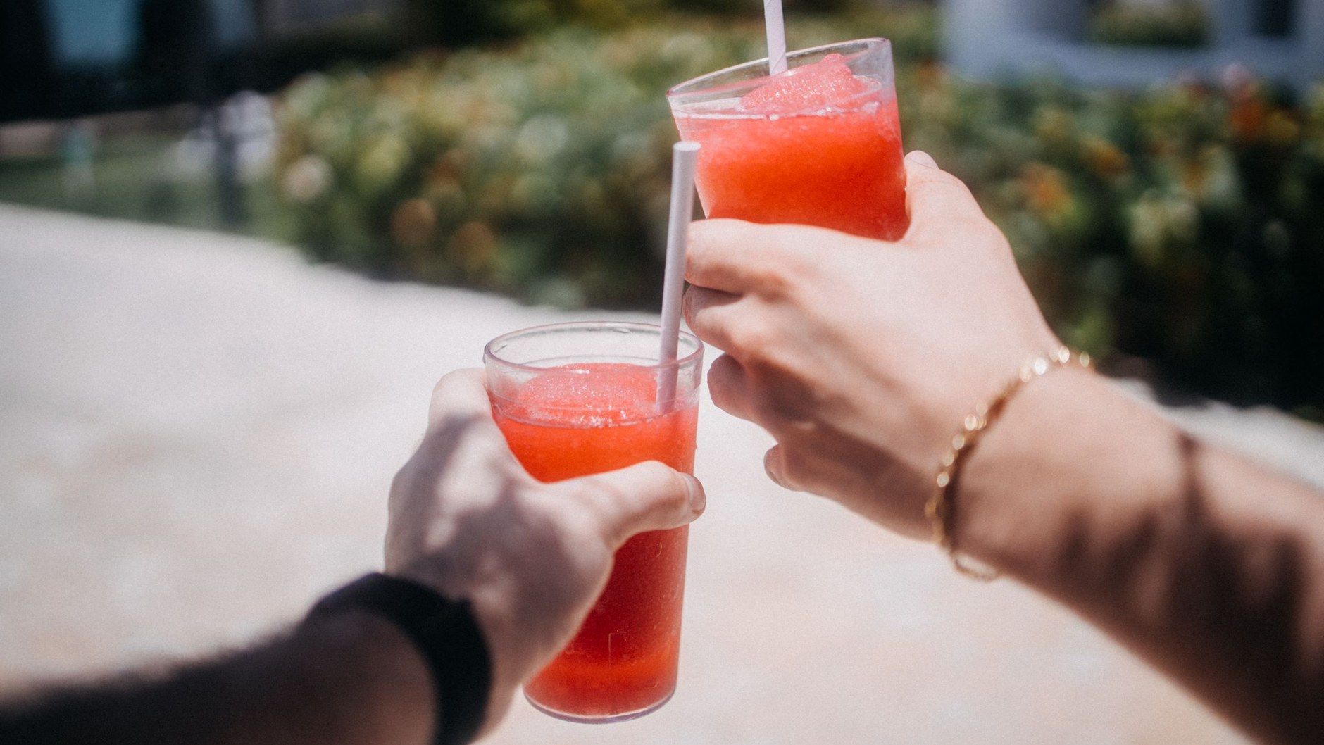 Zwei Hände stoßen mit roten Slush-Getränken im Freien an – Sommererfrischung ohne Zucker