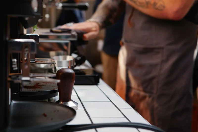 Side view of crop unrecognizable tattooed male worker cleaning electric coffee machine with rag in cafeteria