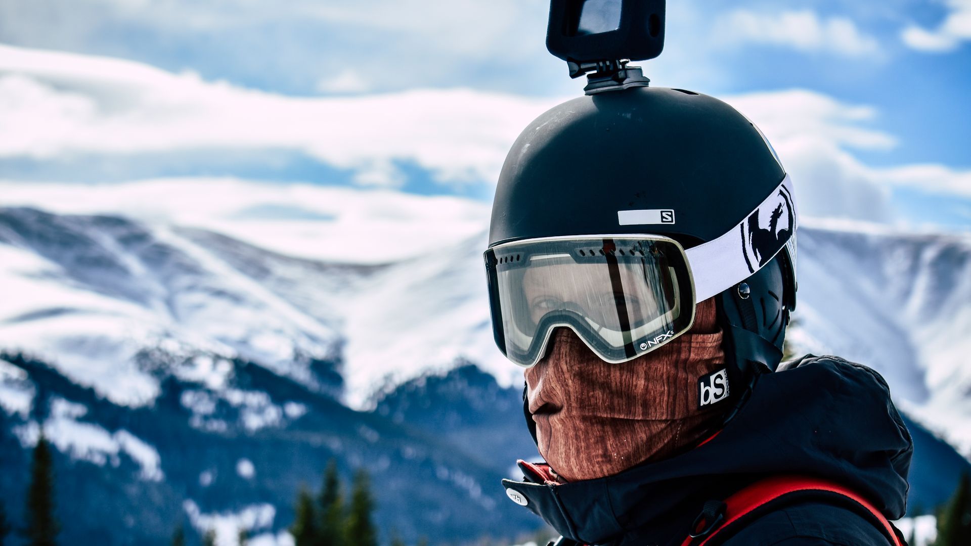 Skifahrer mit Action-Cam auf dem Helm vor verschneiter Bergkulisse