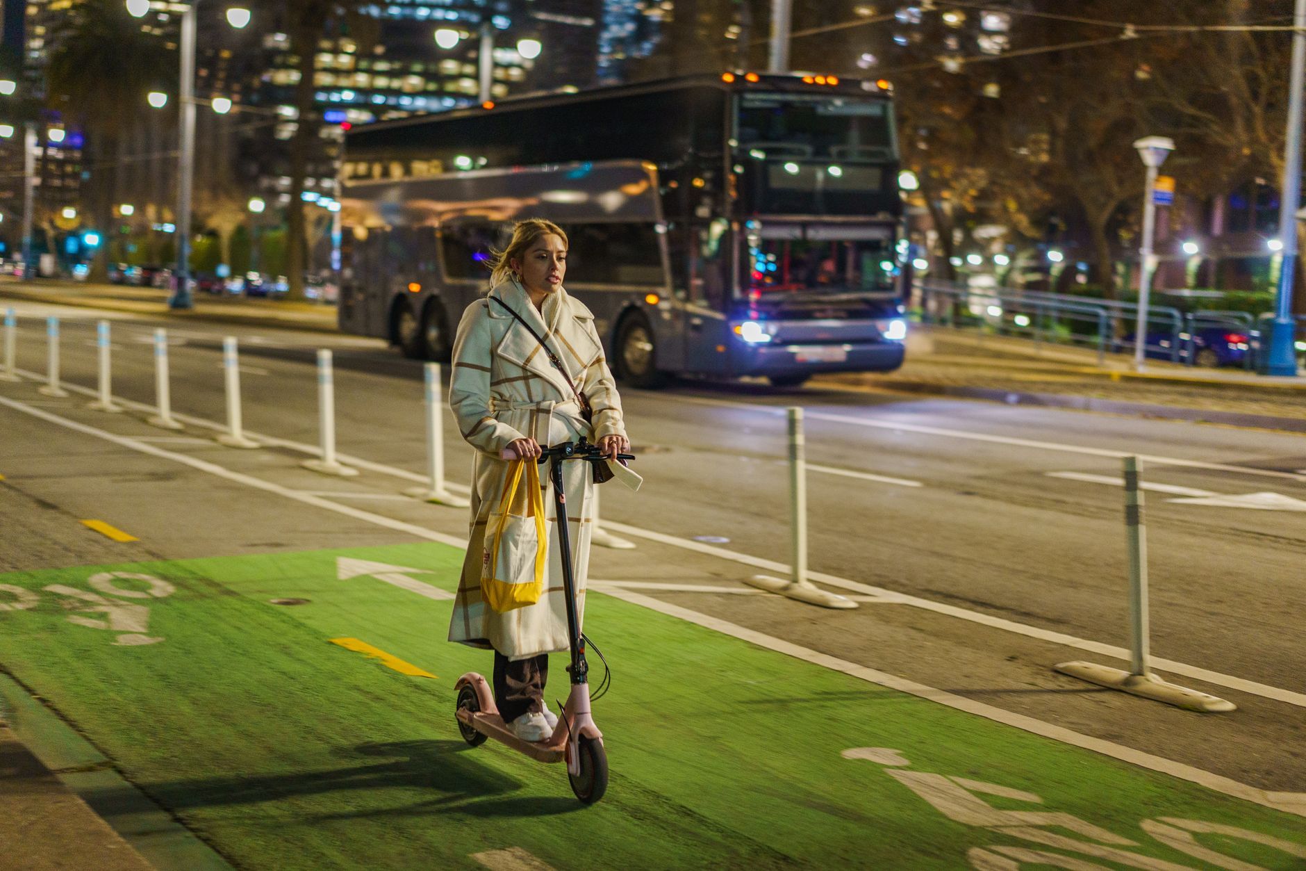 Young woman rides electric scooter in city at night with traffic.