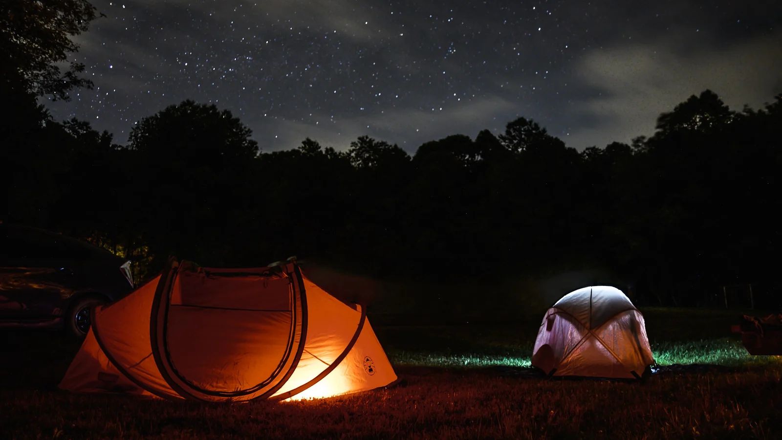 Beleuchtete Zelte auf einem Campingplatz bei Nacht unter Sternenhimmel
